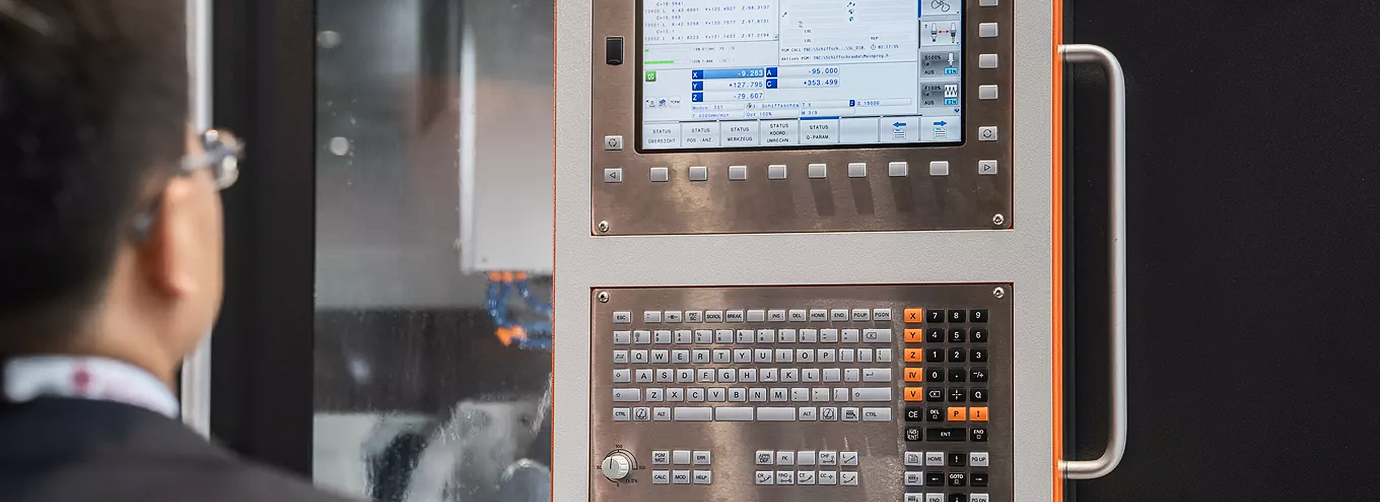 Man in glasses operating a control panel with screen and keypad on industrial machinery.