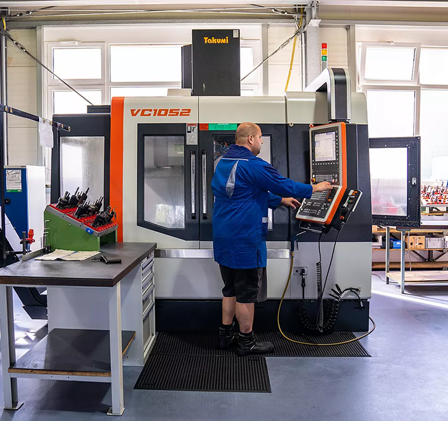 Worker operating a Takumi VC1052 CNC machine in an industrial workshop.