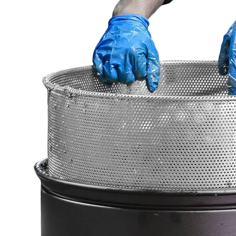 Hands wearing blue gloves holding a perforated metal basket on top of a black cylindrical container.