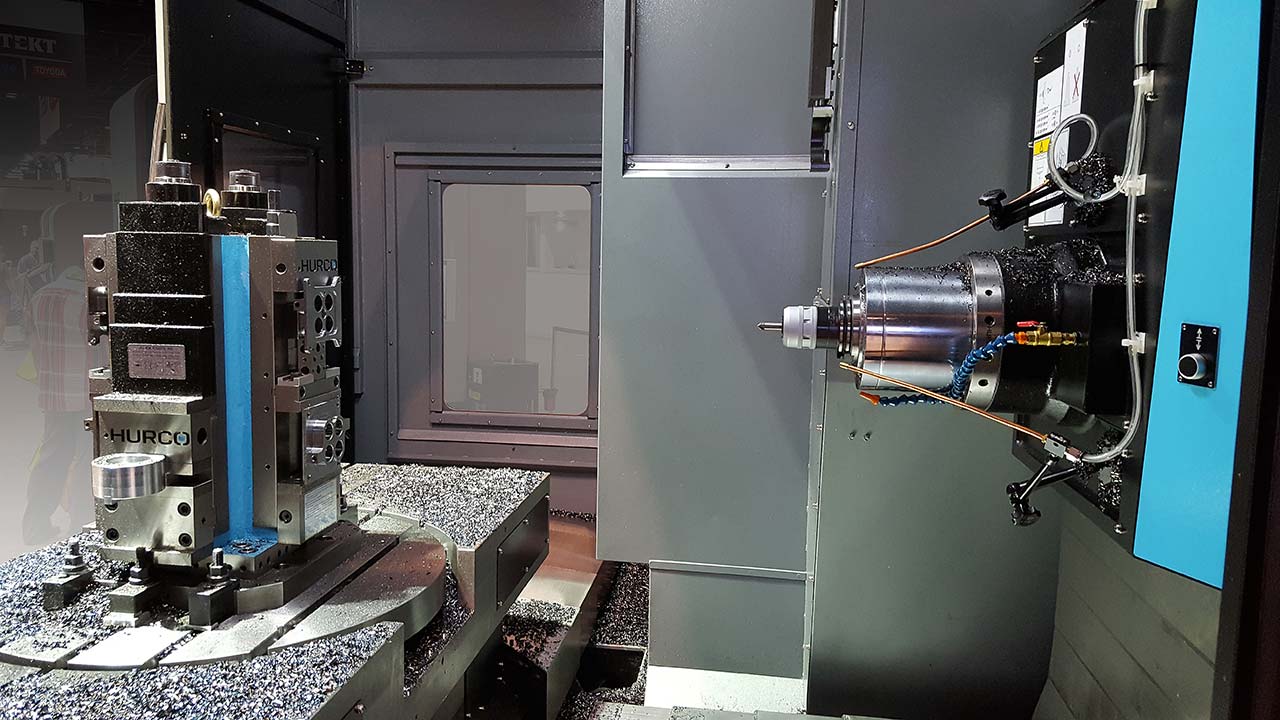 Inside view of a CNC milling machine with metal shavings on rotating worktable and spindle.