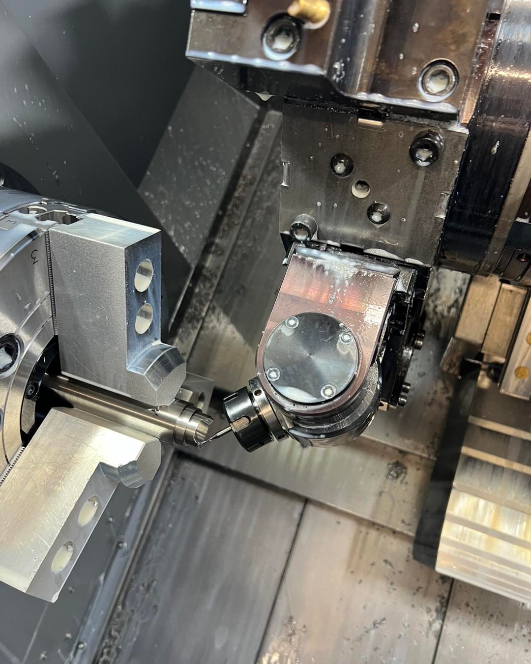 Close-up of a CNC machine tool working on a metal cylindrical part inside a lathe chuck.