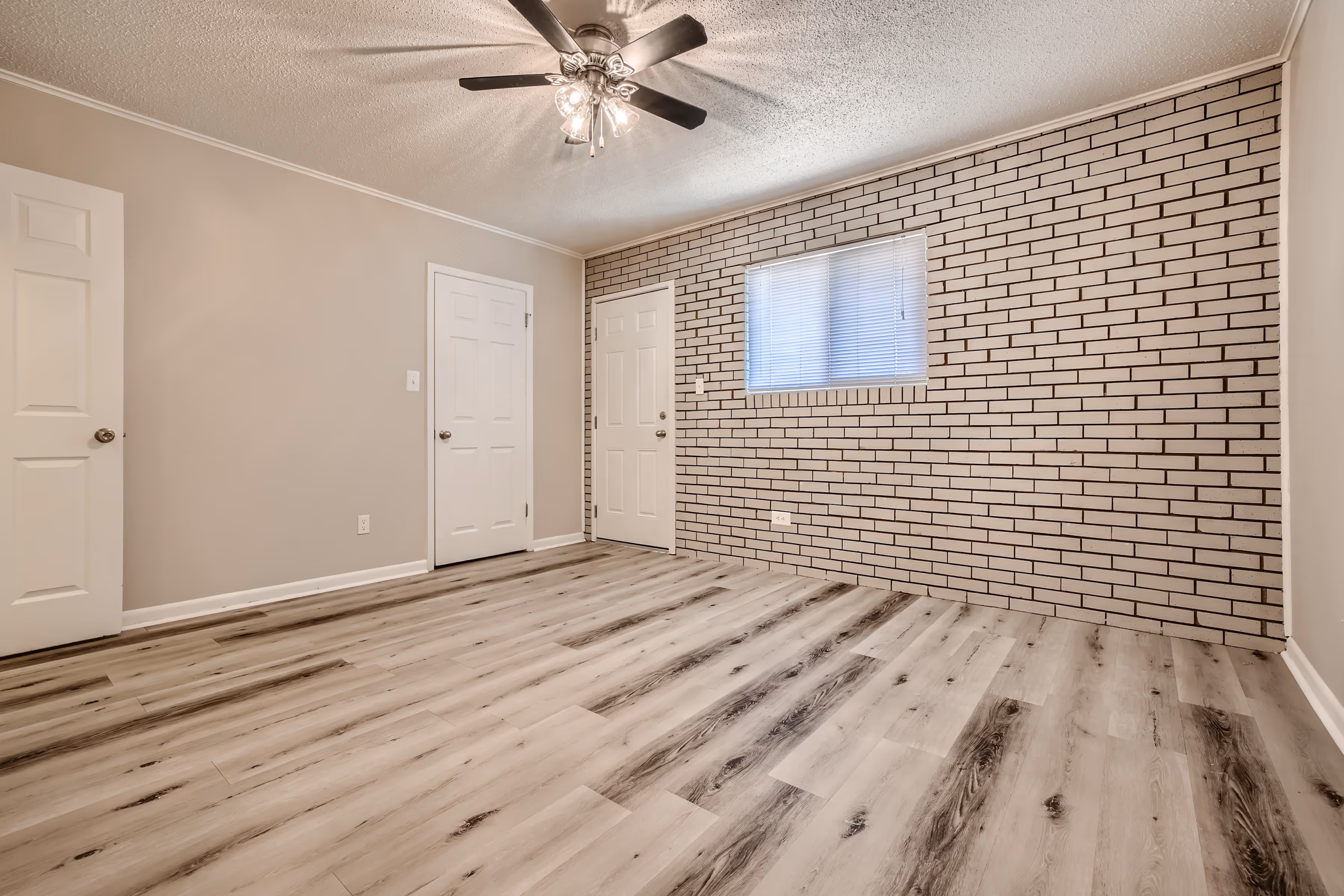 Primary bedroom with ceiling fan and white brick wall