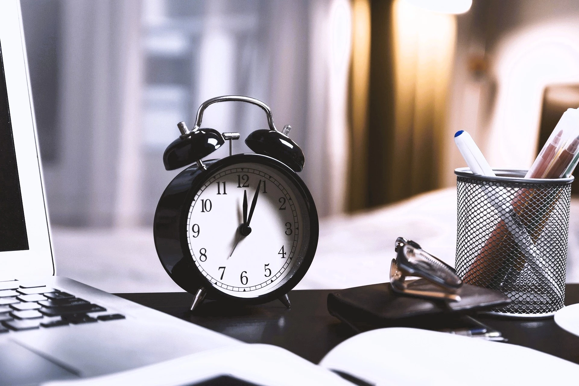 La imagen muestra un reloj despertador sobre un escritorio de trabajo y transmite la percepción del paso del tiempo