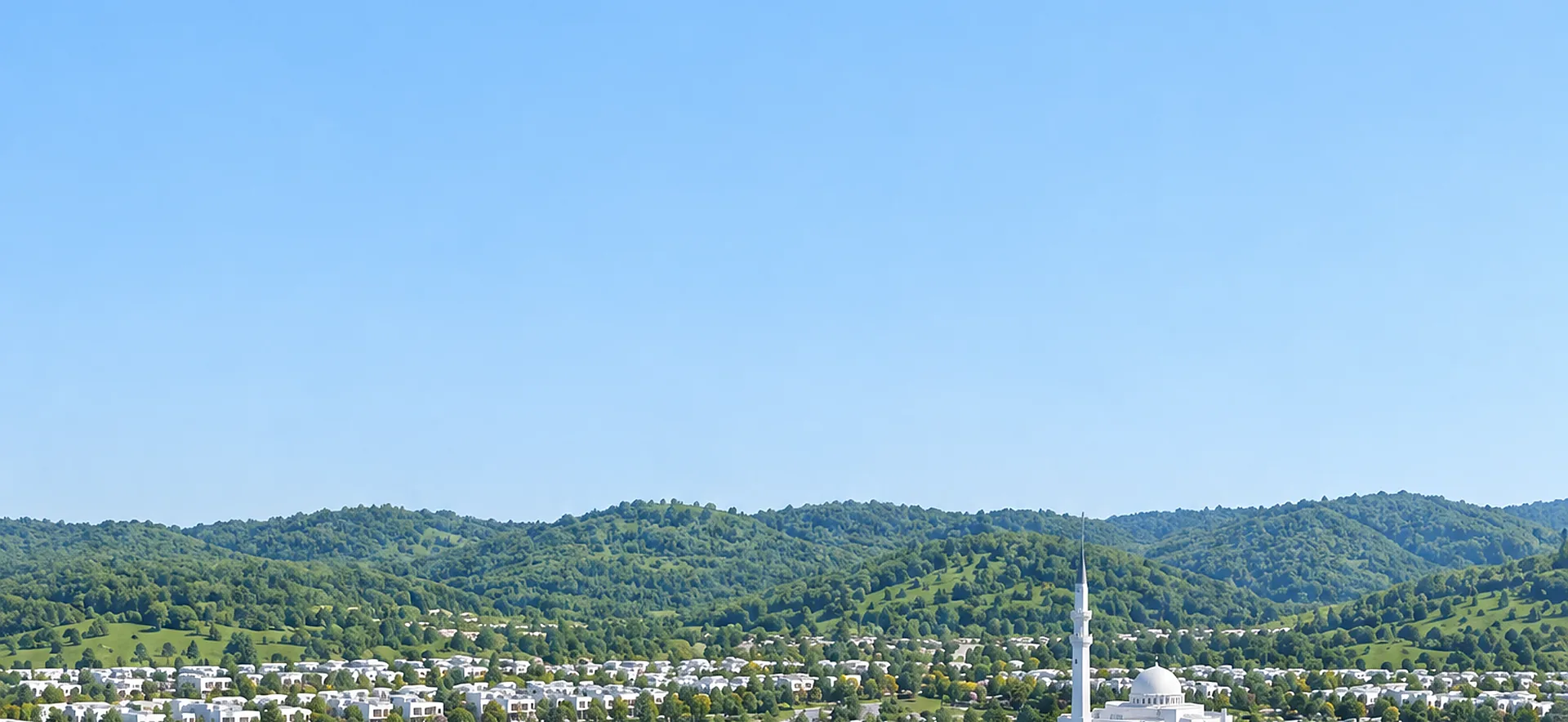 Aerial view of New Airport City Islamabad with white homes, tree-lined streets, a lake and green hills under a clear blue sky