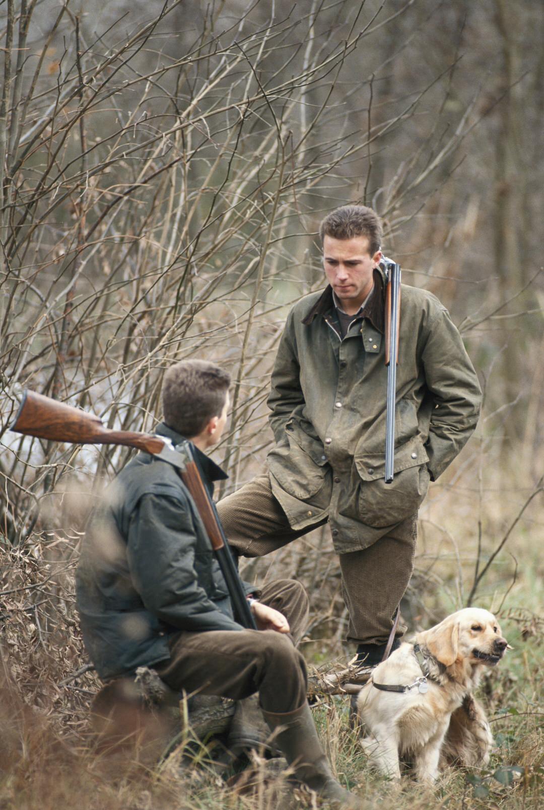 Two hunters with rifles and a dog in a winter forest setting