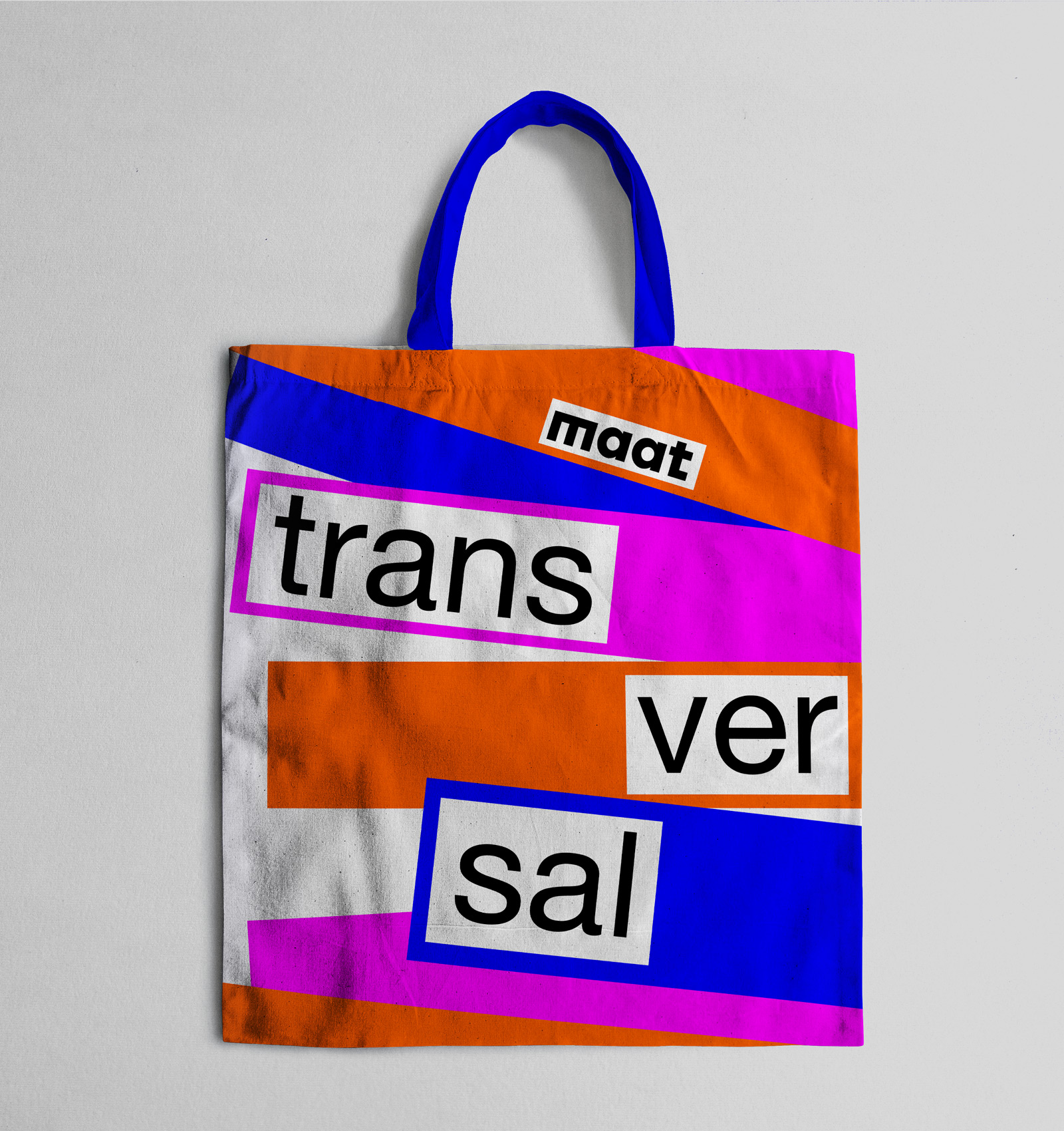 Colorful tote bag with geometric orange, pink, and blue shapes and the words 'maat trans versal' printed in black on white rectangles.
