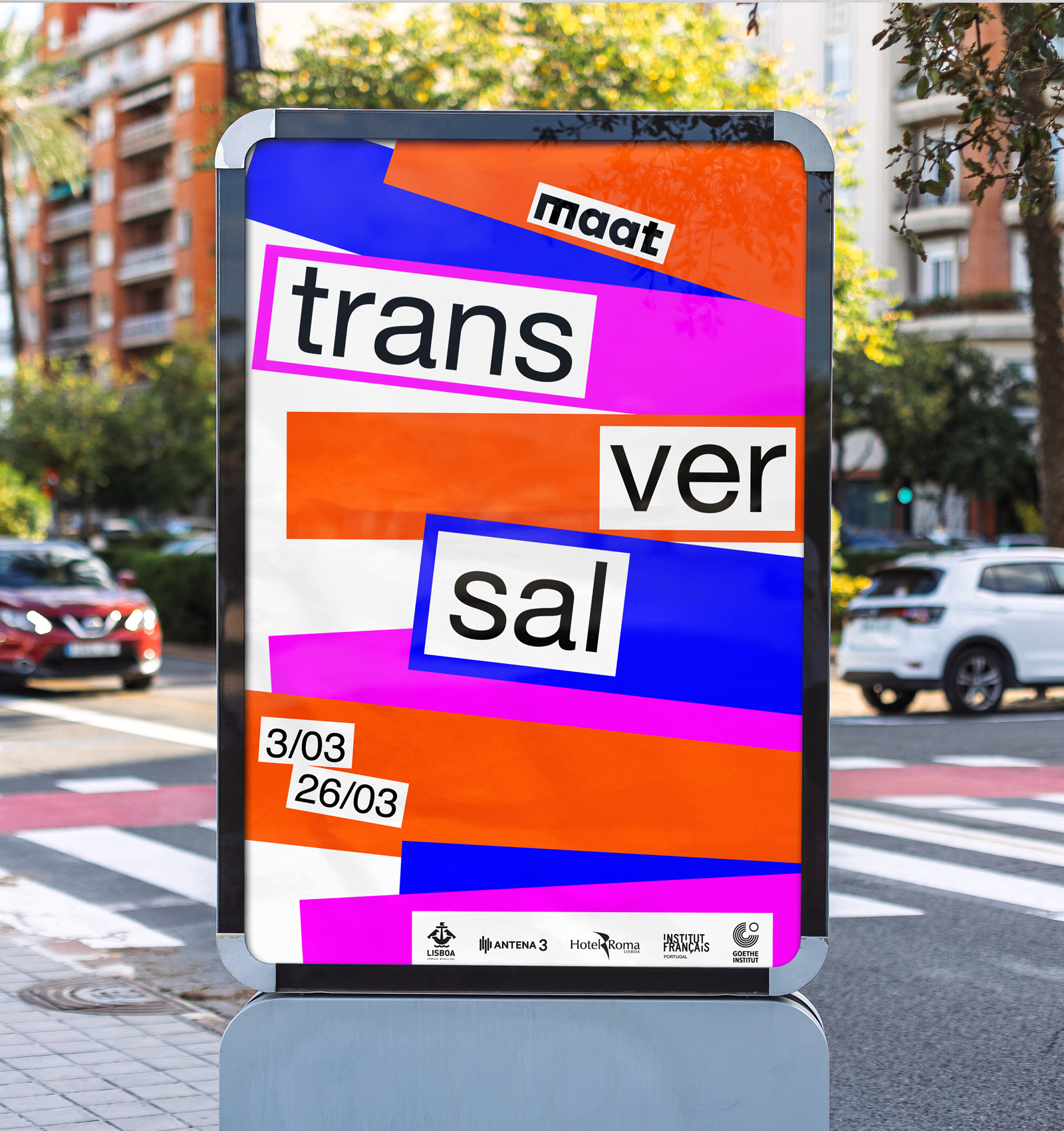 Colorful street poster with the text 'maat transversal' and dates 3/03 to 26/03, displayed near a crosswalk on an urban street.