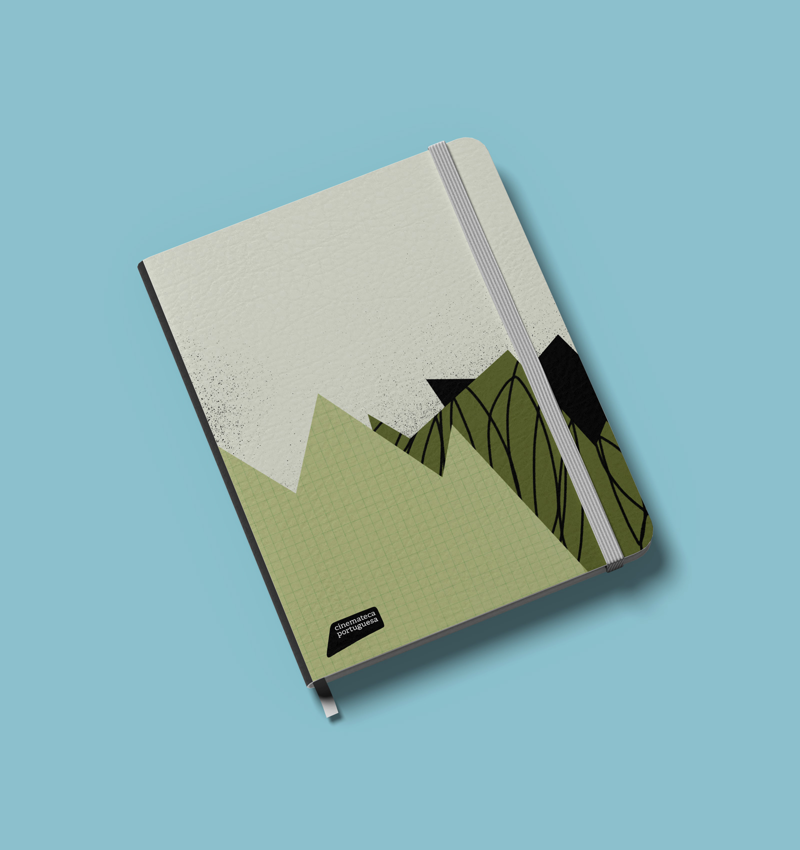 Closed notebook with a green and beige abstract mountain design and a gray elastic band on a blue surface.