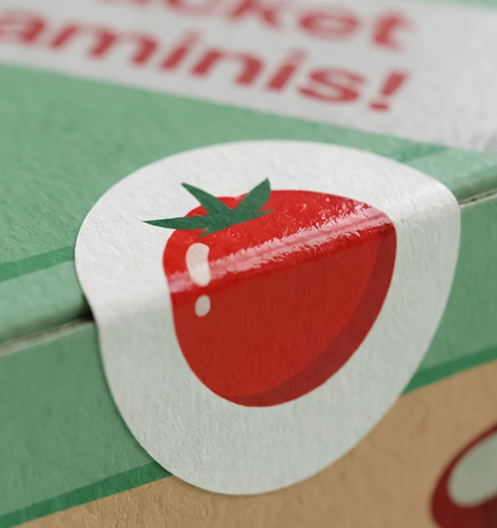 Close-up of a round sticker with a red tomato illustration sealing a green box.