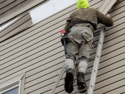Siding being replaced by a worker on a ladder