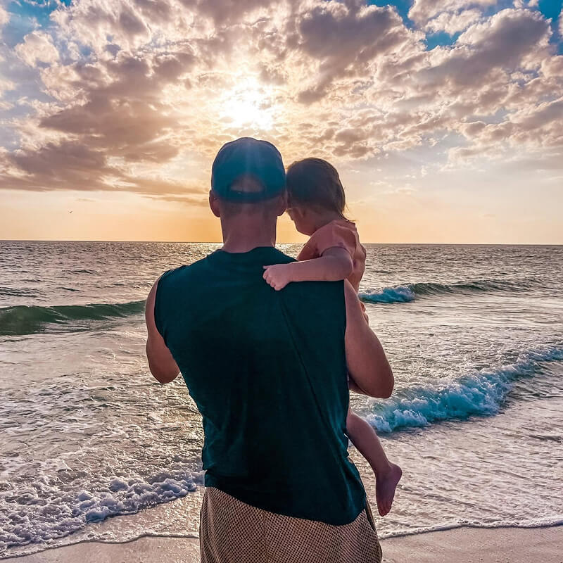 Jeremiah Stogsdill from Brothers Who Roof, on a beach overlooking the sunset over the ocean with his daughter