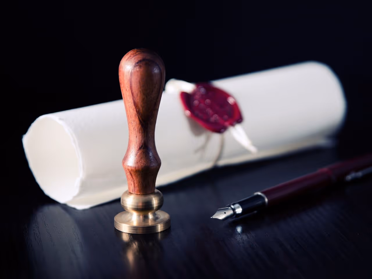 Pergamino enrollado con sello de cera roja, pluma estilográfica y sello de madera, que representa la autenticidad y la documentación oficial.