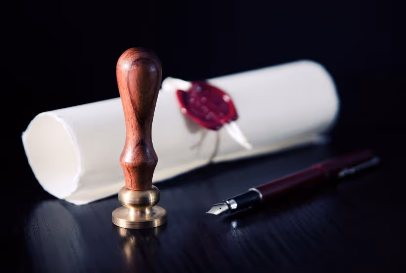 Rolled parchment with a red wax seal, fountain pen, and wooden stamp, representing authenticity and official documentation.