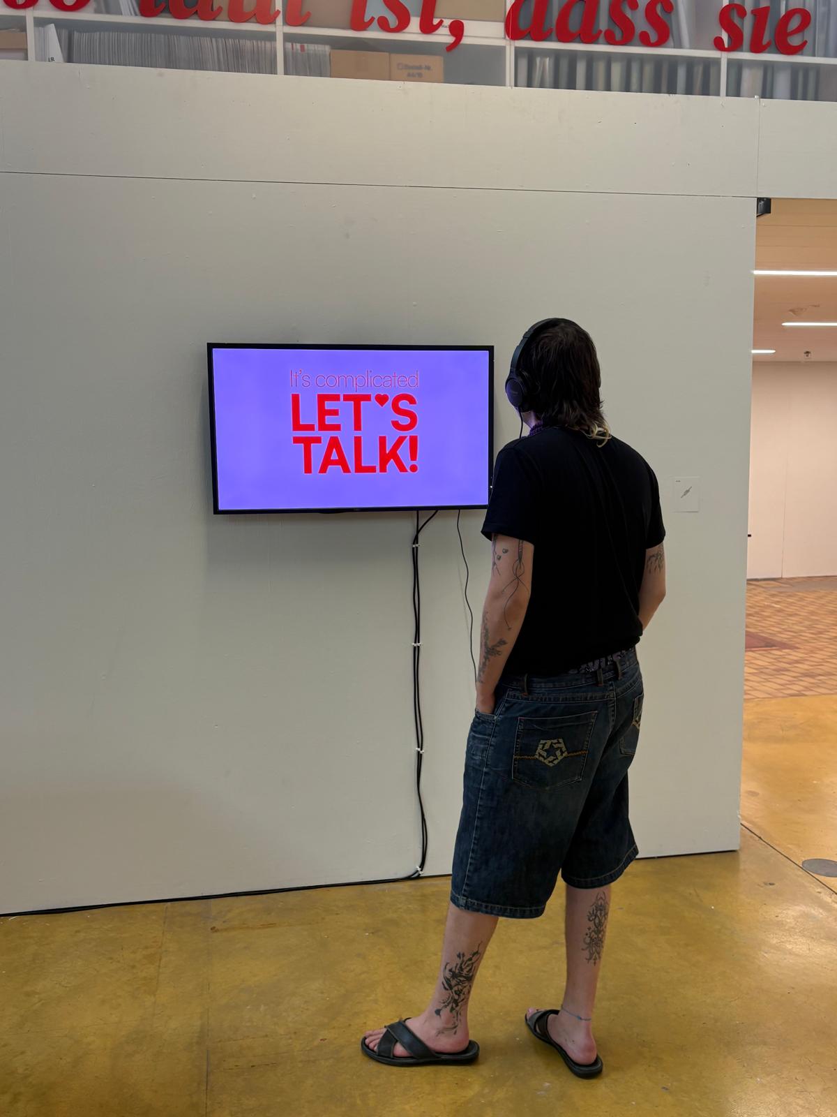 Eine Person steht vor einem Bildschirm, darauf steht das Logo "let's talk". 