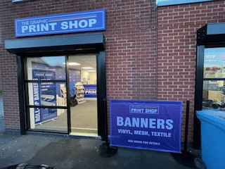 Entrance of a The Graphic Print Shop with signs advertising banners in vinyl, mesh, and textile materials.
