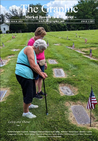 Two elderly women standing by a gravesite in a cemetery decorated with small American flags.