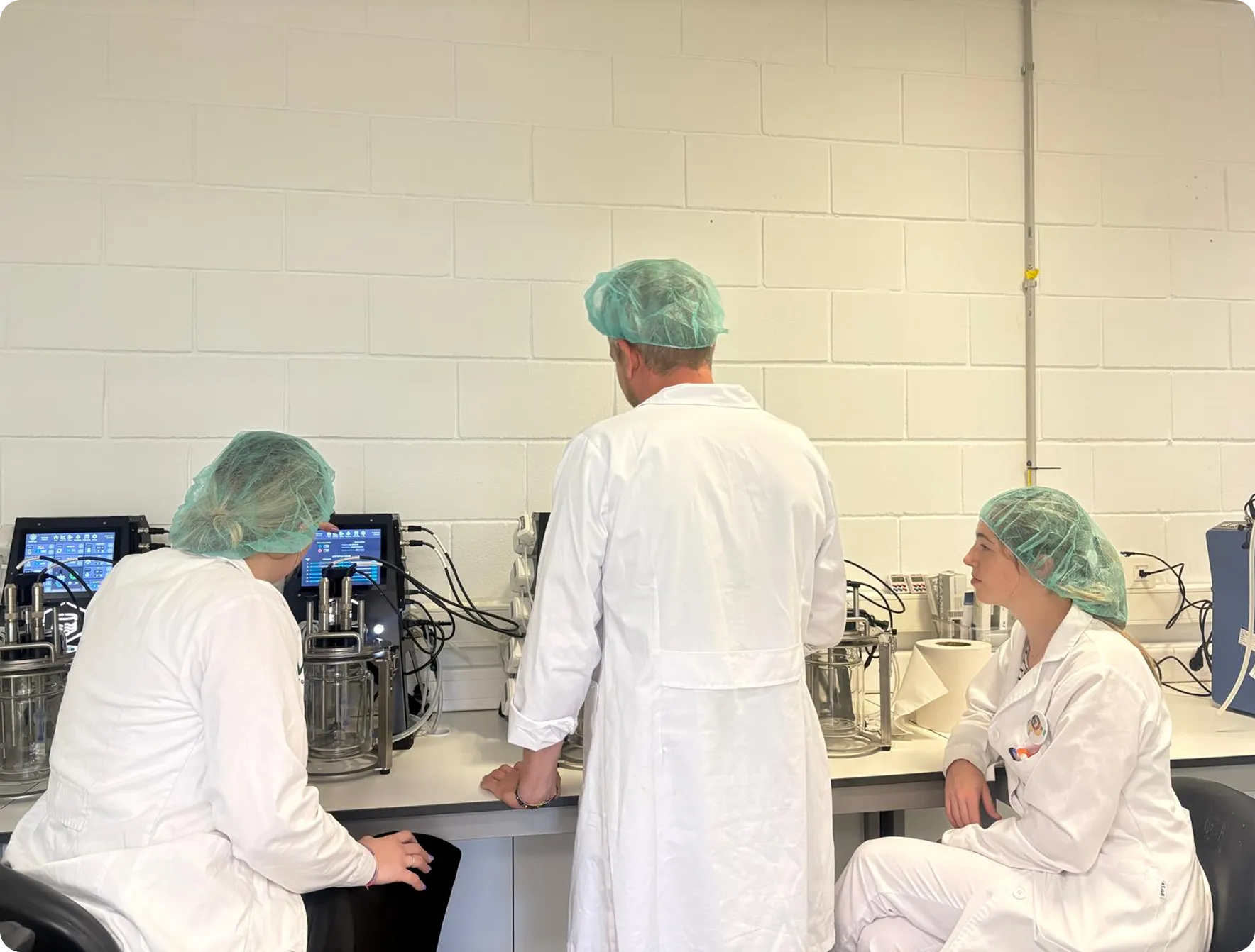 MOA laboratory researchers in white coats and hair caps working with fermentation equipment in sterile facility