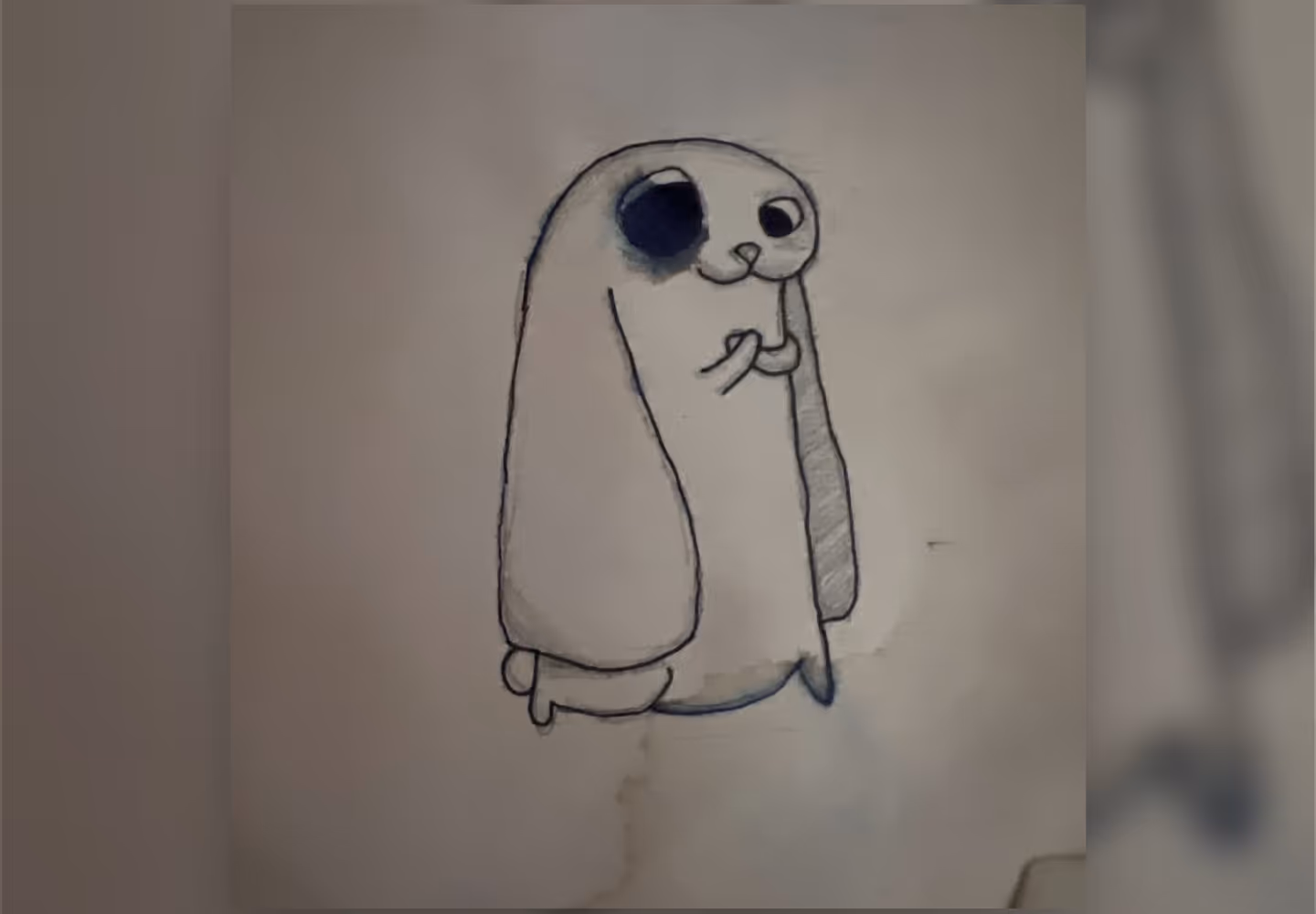 Sketch of a small, rounded animal with floppy ears, one dark spot around its eye, and tiny front paws.