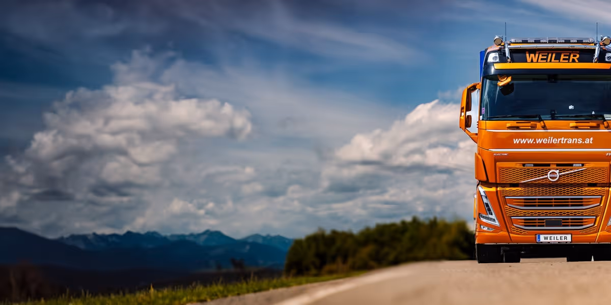 Professionelle Unternehmensfotografie und Fahrzeugfotografie von Visual Artisan: Ein moderner orangefarbener WEILER Transport & Lagerlogistik LKW auf der Straße unter dramatischem Himmel. Perfekt für Logistikunternehmen und Speditionen, die ihre Flotte und Marke visuell stark präsentieren möchten. Ihr Experte für beeindruckende Business-Visualisierungen im Transportwesen.