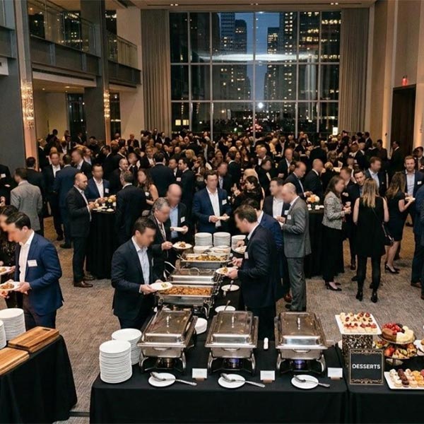 Catering captain coordinating servers at a corporate reception — food stations and bar setup with guests in the background.
