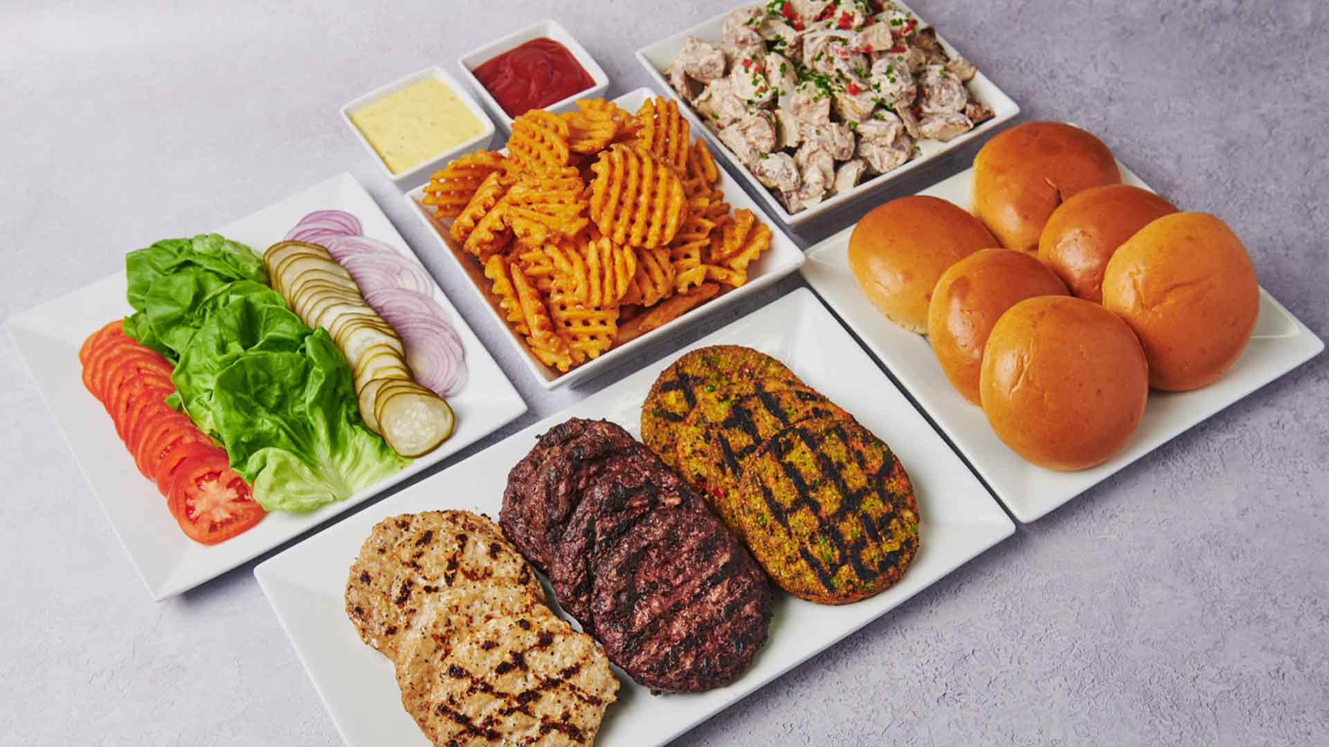 A build-your-own burger package featuring beef burgers, turkey burgers, and veggie burgers served with soft brioche buns and classic toppings including lettuce, tomato, onions, and pickles. Served with roasted Caesar potato salad, waffle fries, ketchup, and Metro Secret Sauce.
