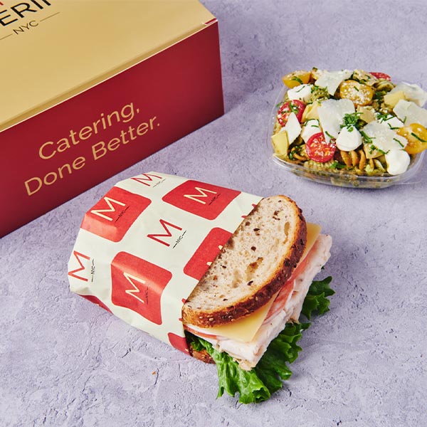 Metro Catering sandwich with turkey, cheese, lettuce and tomato beside a fresh salad and branded “Catering, Done Better” box