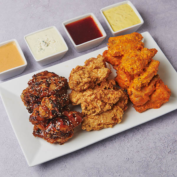 Platter of crispy chicken wings featuring BBQ glazed, classic fried, and Buffalo flavors, served with a selection of dipping sauces including blue cheese, ranch, honey mustard, and barbecue.