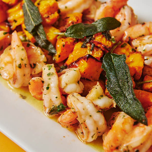 Sautéed shrimp with roasted squash and crispy sage leaves on a white platter from Metro Catering’s fall seasonal menu.
