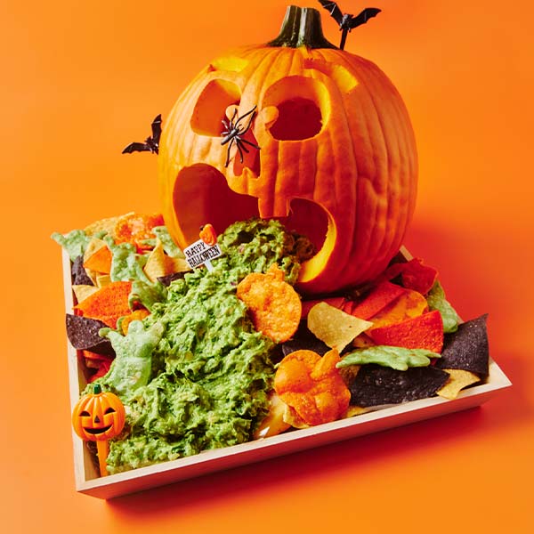 Carved Halloween pumpkin with guacamole spilling from its mouth, surrounded by colorful tortilla chips on a Metro Catering platter.