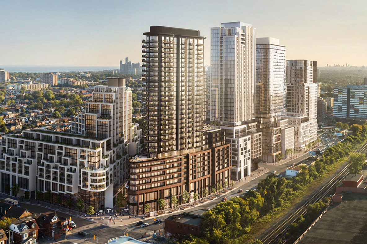 Aerial view of a modern urban development featuring multiple high-rise residential and mixed-use buildings with contemporary architecture, surrounded by tree-lined streets and a sprawling cityscape under a clear sky.