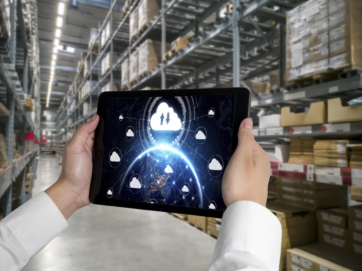 Profissional utilizando um tablet em um armazém logístico automatizado, com uma interface gráfica de computação em nuvem conectando diferentes pontos da cadeia de suprimentos. O cenário destaca tecnologias de Cloud Computing aplicadas à logística, incluindo gerenciamento de estoque, monitoramento em tempo real, integração de sistemas, análise de dados, rastreabilidade de produtos e otimização de operações. A fotografia representa a transformação digital no setor logístico, com foco em eficiência operacional, escalabilidade e conectividade empresarial.