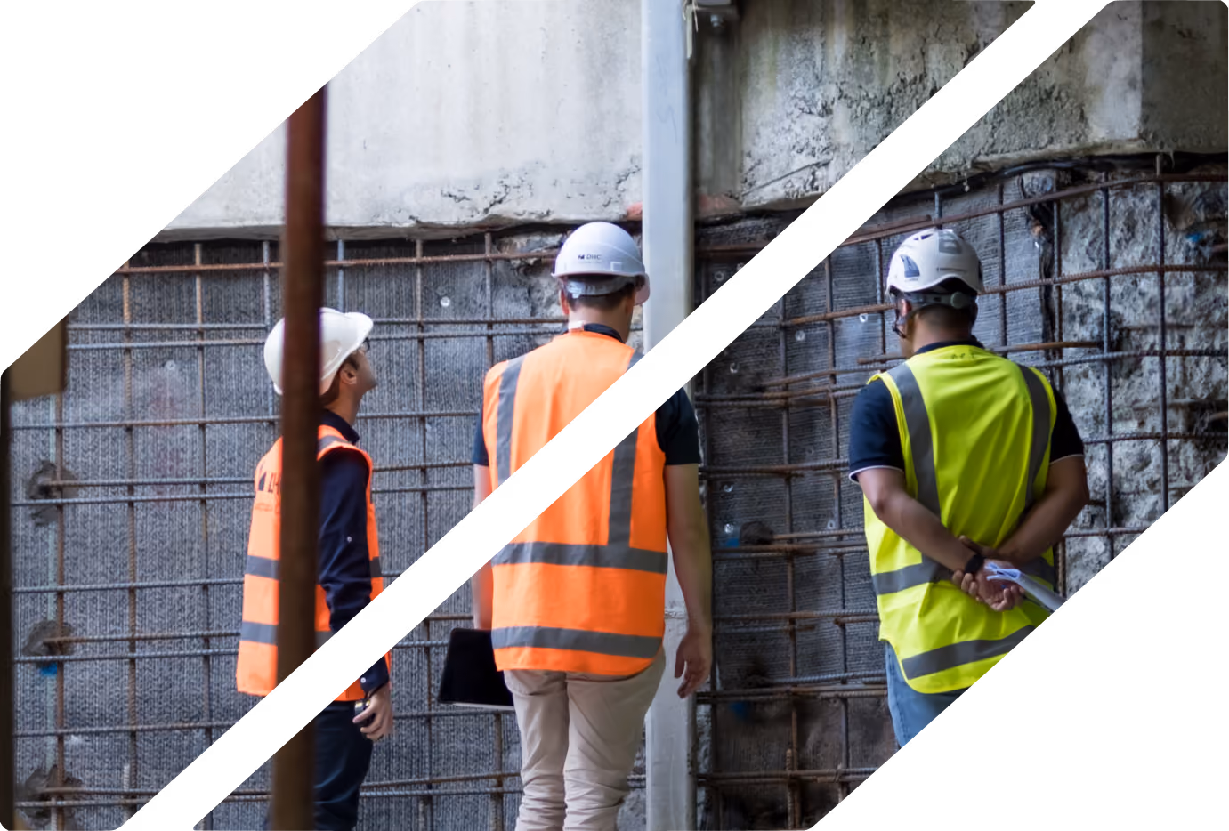 Three construction workers wearing hard hats and high-visibility vests, standing and observing a concrete wall with exposed rebar inside a building under construction.