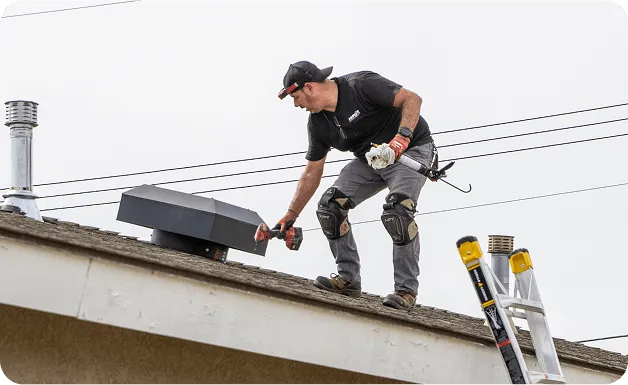 Roofer working on roof with tools, wearing safety gear and cap
