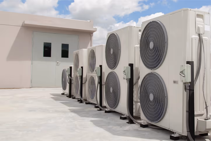 Multiple air conditioning units lined up outside a building on a sunny day