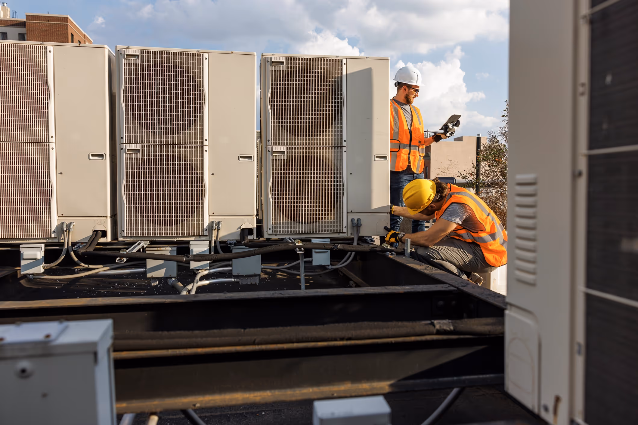 Technicians in safety vests inspect large HVAC units on commercial building rooftop