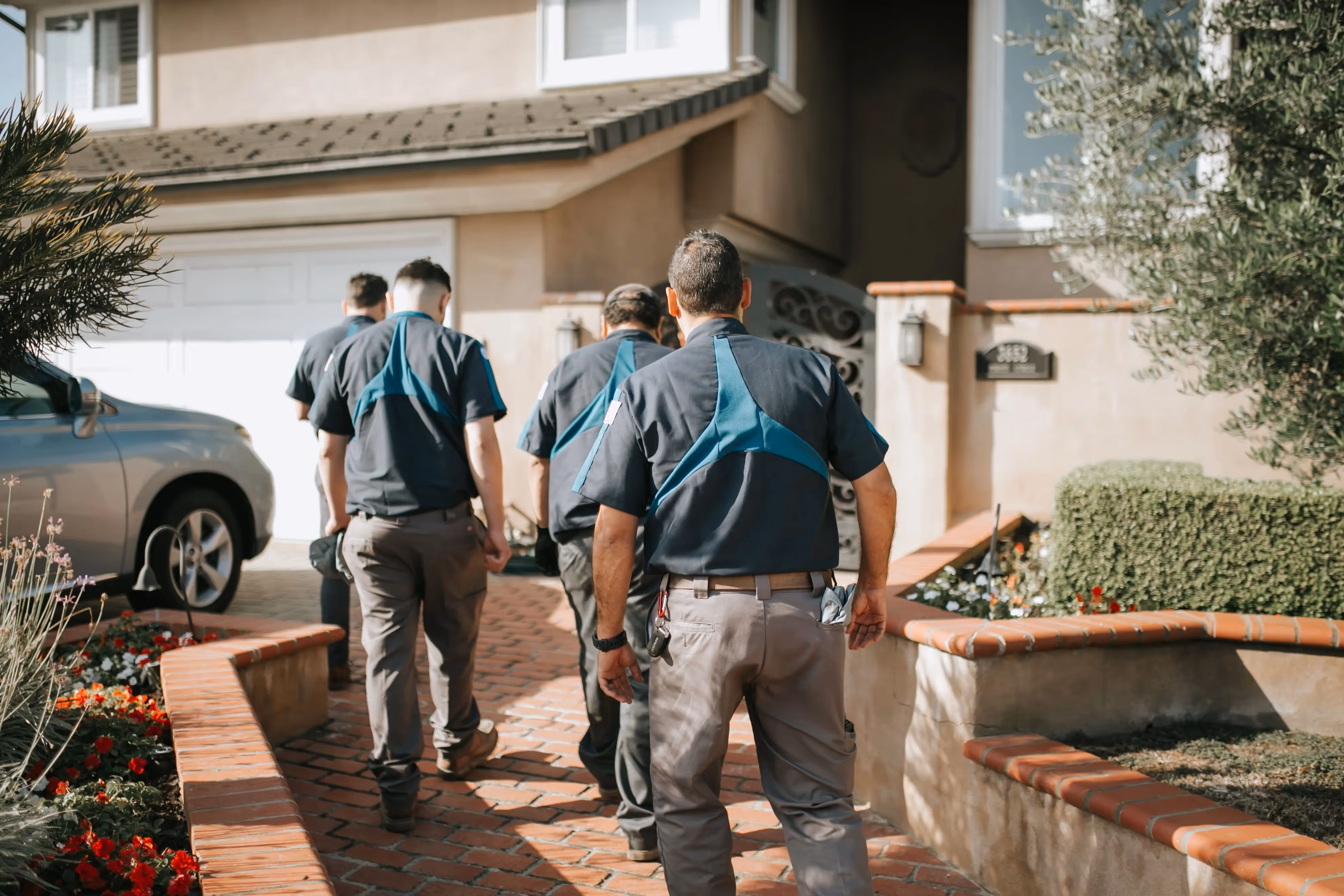 Workers in blue and gray uniforms walking along brick pathway near house