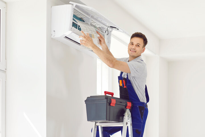 Technician repairing air conditioning unit on ladder with toolbox