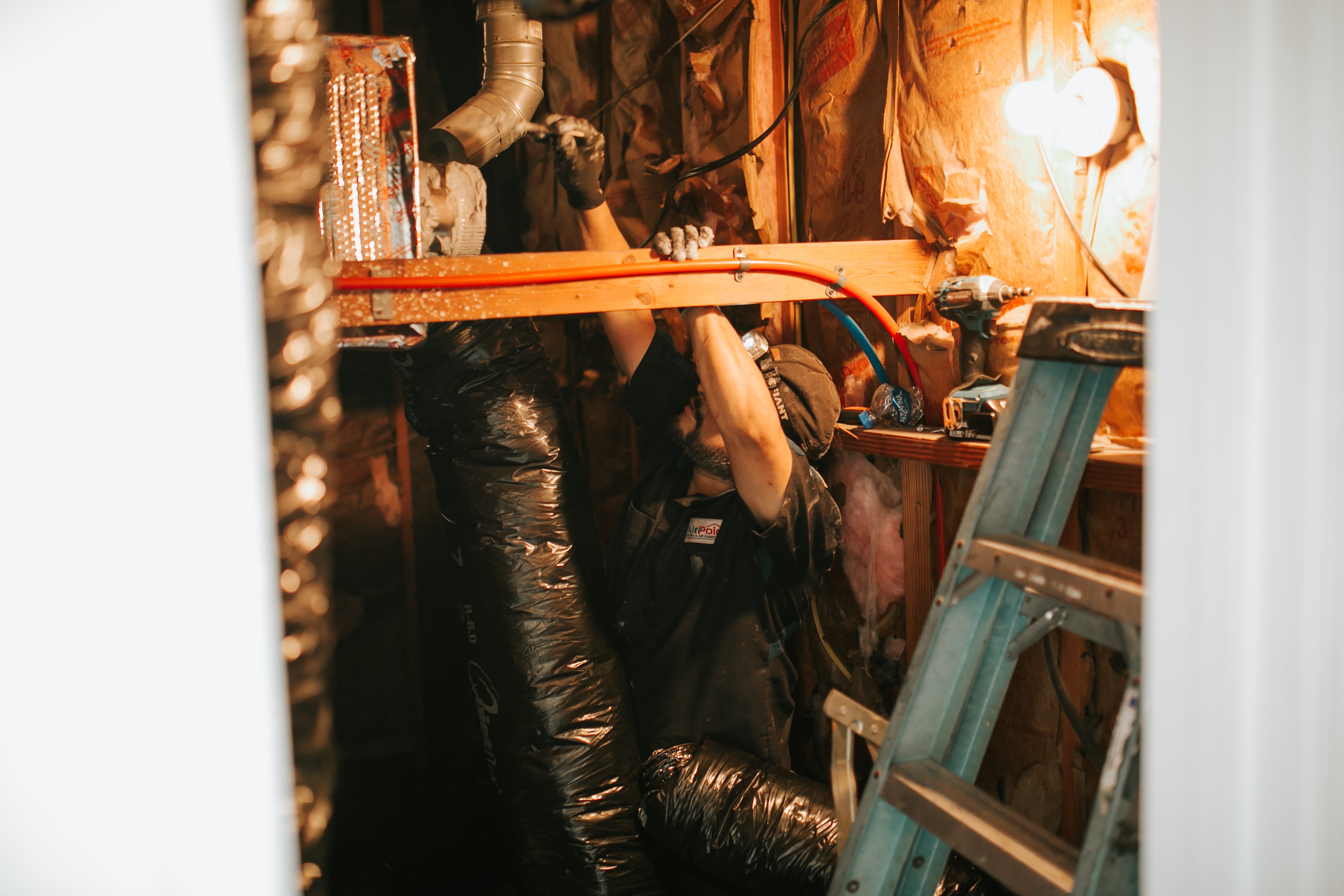 Worker in tight space with pipes, ladder, and wrapped insulation materials