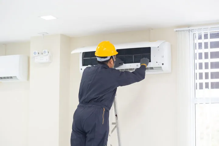 Technician in yellow hard hat repairing air conditioning unit on wall