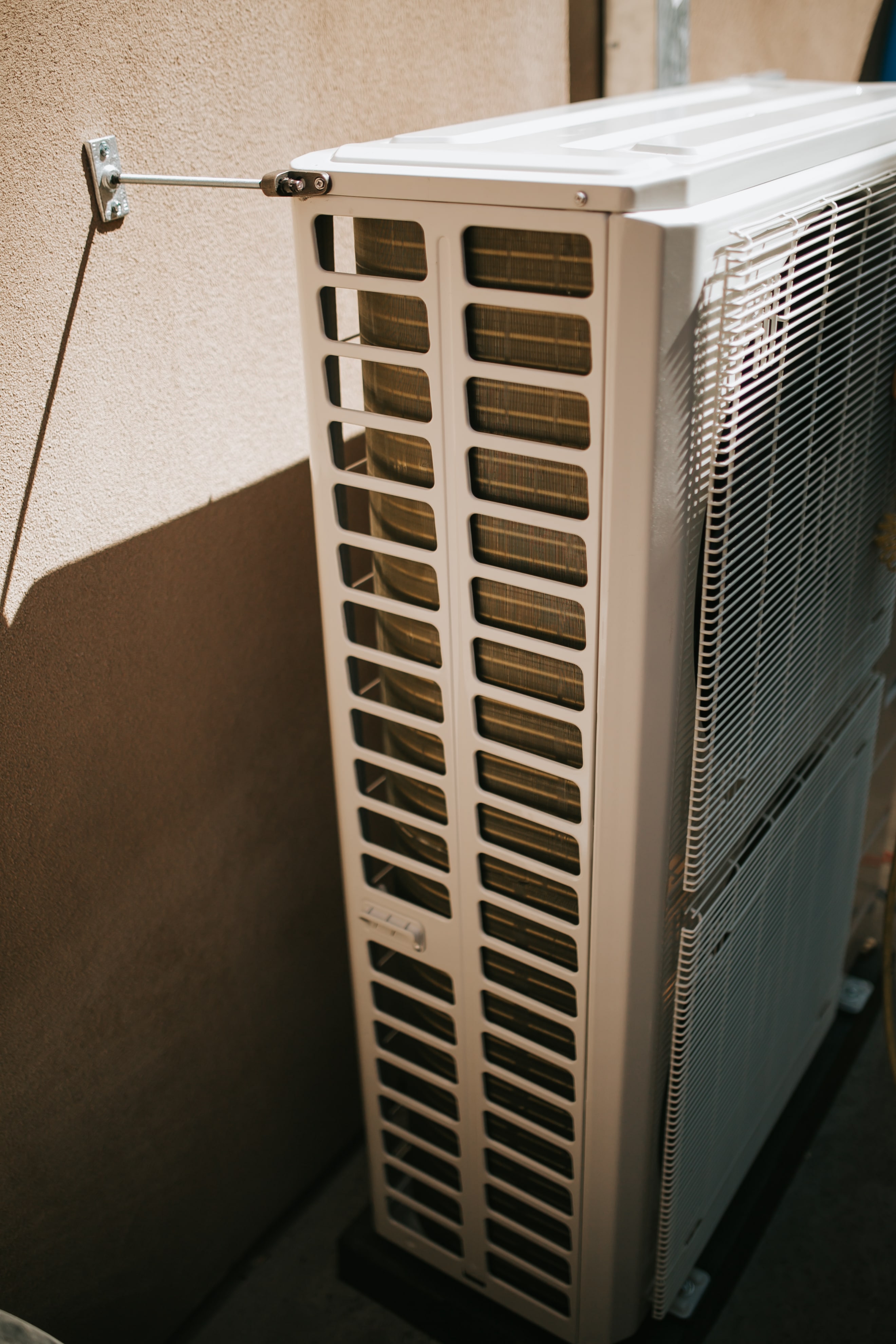 Outdoor air conditioning unit mounted on beige wall with metal bracket