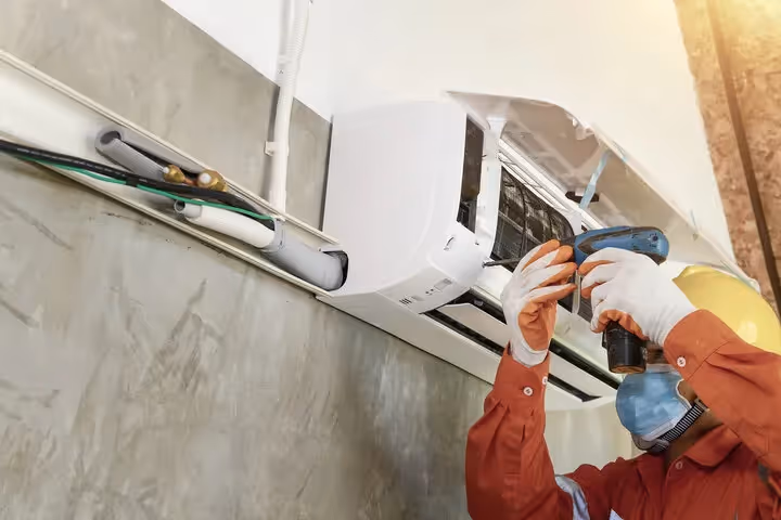 Technician in safety gear repairing and cleaning air conditioning unit