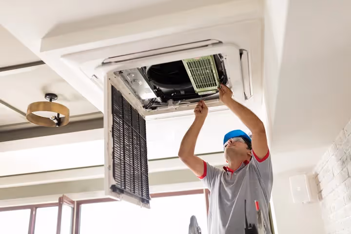 Technician repairing ceiling-mounted air conditioning unit with open panel