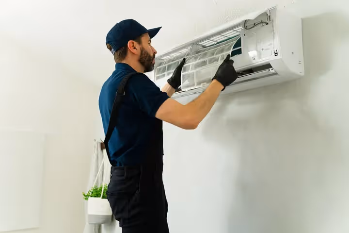 Technician in blue uniform installing or repairing a wall-mounted air conditioner