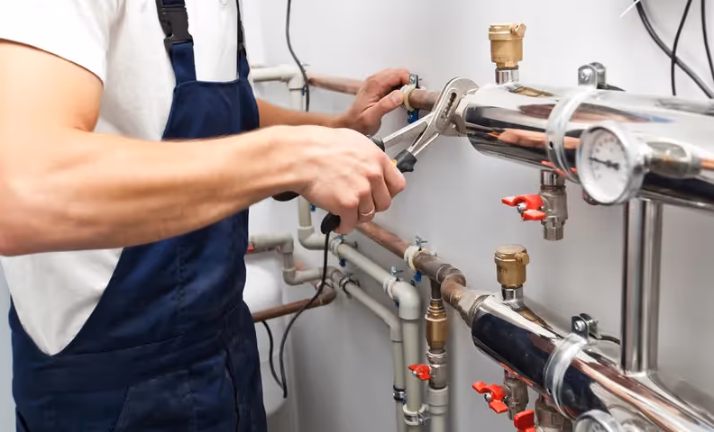 Plumber adjusting pipes and valves on industrial heating or water system