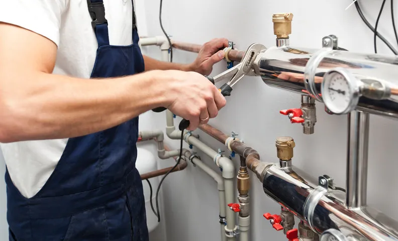 Plumber adjusting pipes and valves in industrial heating or water system