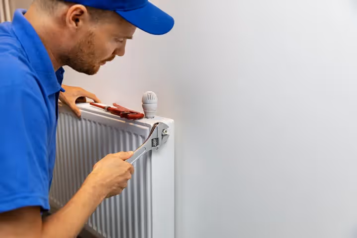 Technician in blue uniform repairing radiator with wrench and pliers