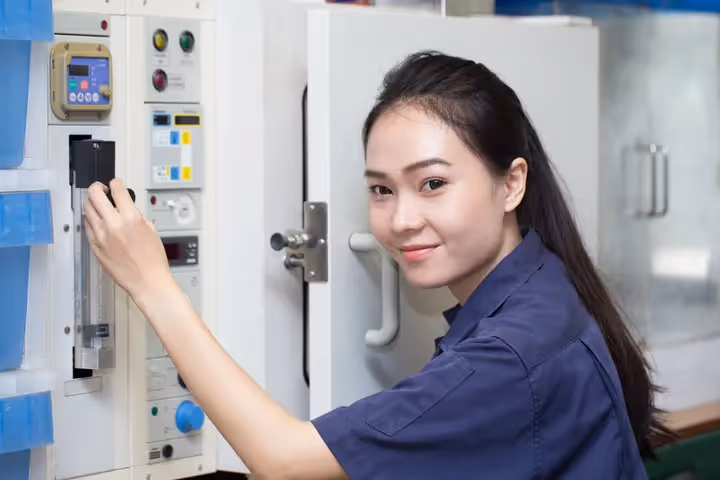 Female technician operating industrial control panel in blue uniform