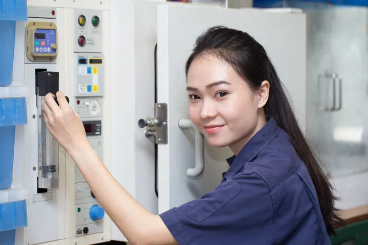 Female technician operating industrial control panel in blue uniform