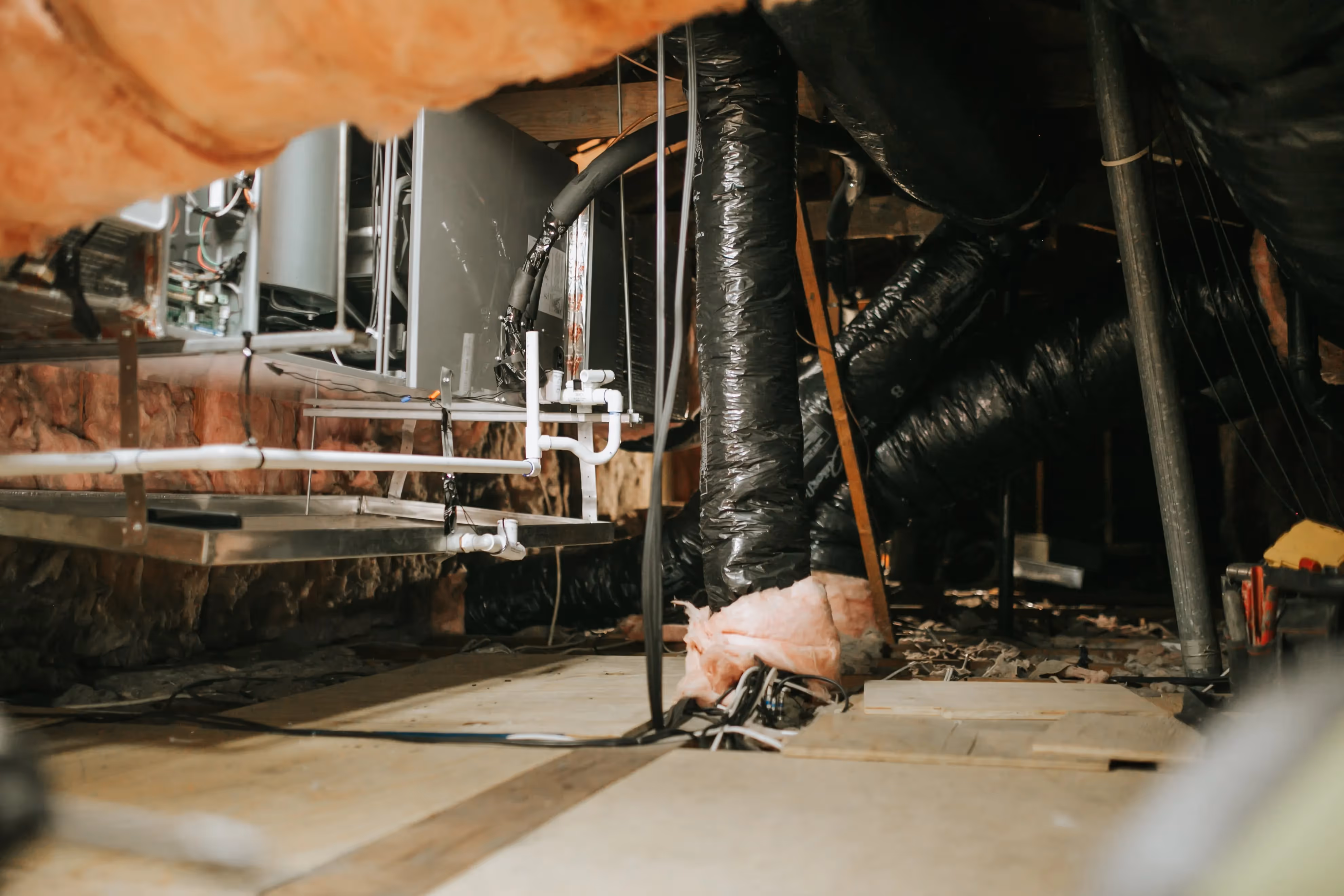 Cluttered crawl space with mechanical equipment, pipes, and insulation