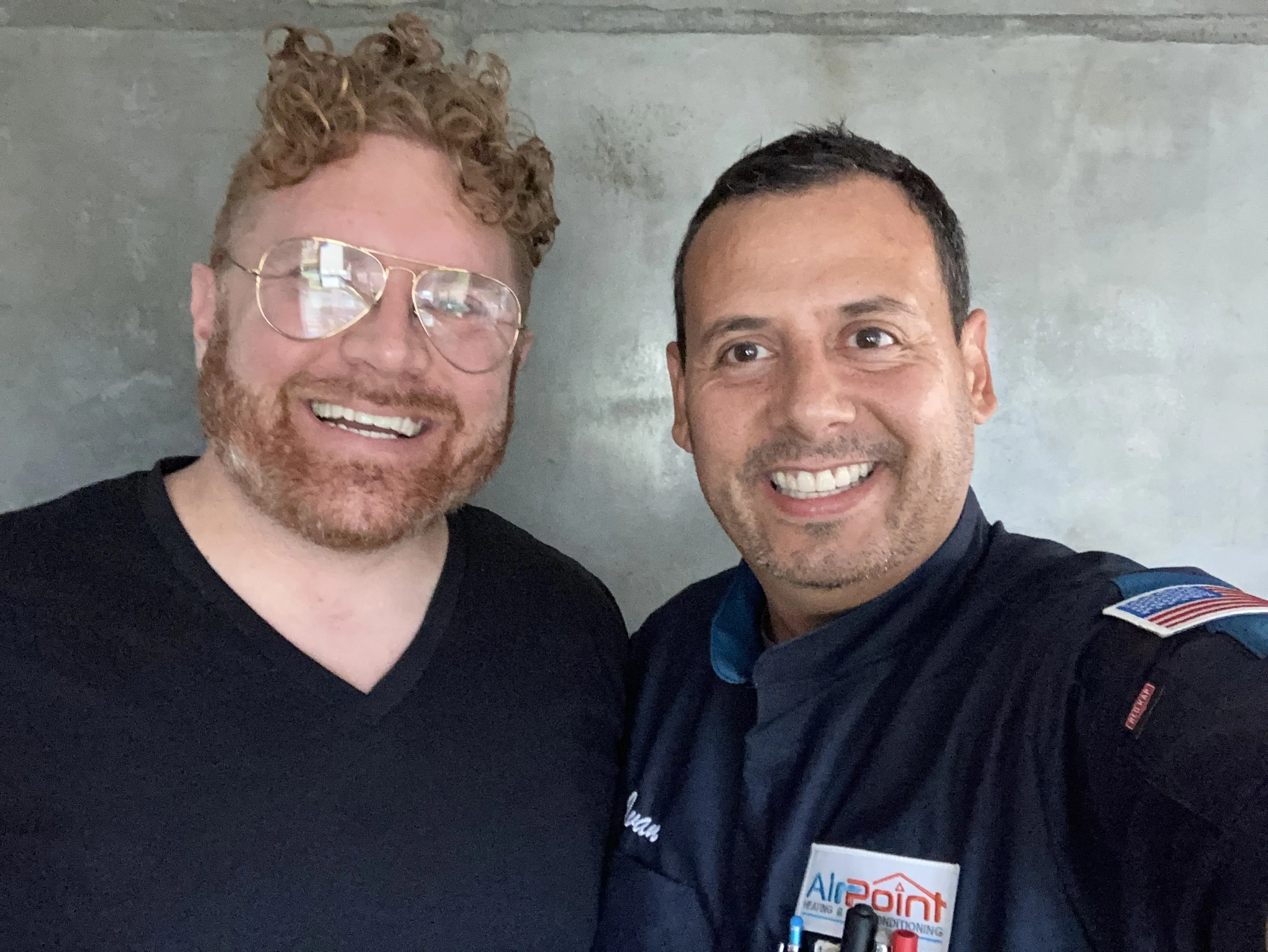Two smiling colleagues posing together in front of a gray wall